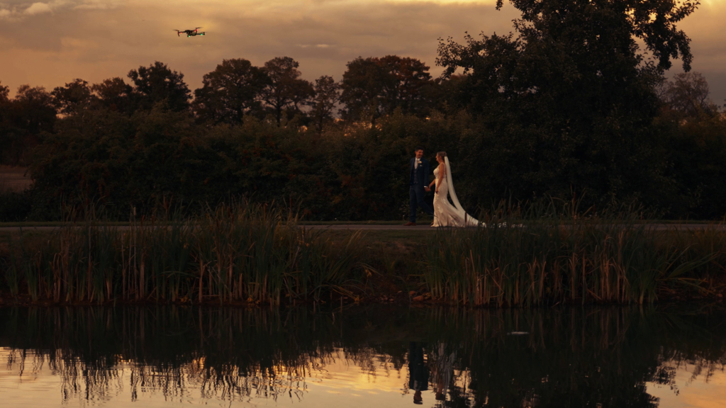 Drone capturing wedding couple walking by the lake at sunset