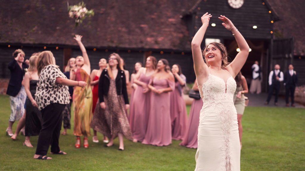 Bouquet toss on lawn at wedding at Lains Barn, Oxfordshire